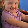 child, toddler, smiling, purple_shirt, blonde_hair, blue_eyes, seat, black_shorts, happy, portrait, indoor, person, cute, young_child, casual_clothing, fun, joy, arm, hair, face