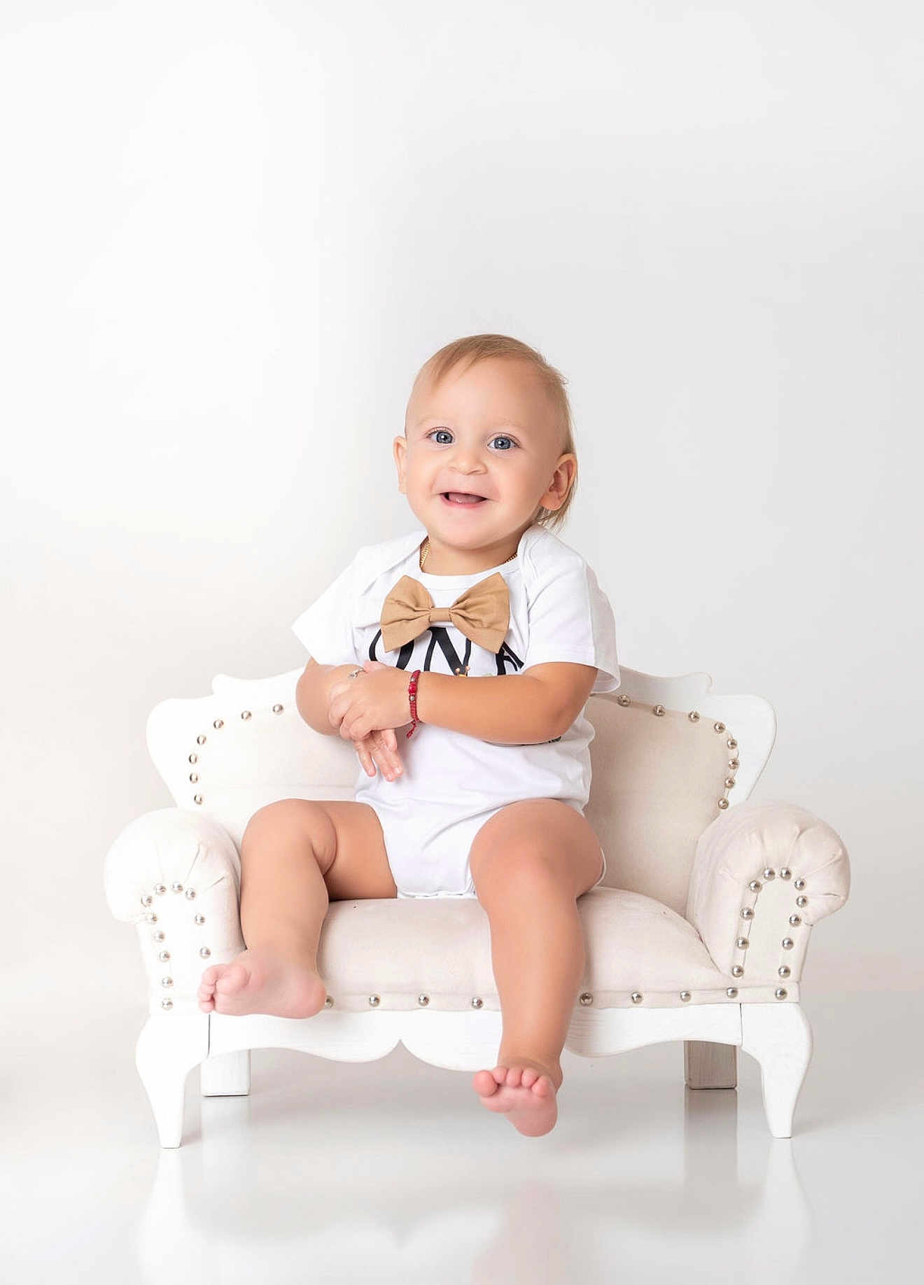 Mateo joined the competition — help win amazing prizes! baby, child, smiling, onesie, bow_tie, couch, white_background, happy, sitting, portrait, cute, indoor, feet, furniture, infant, person, studio, toddler, fashion, cute_face