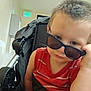 toddler, child, sunglasses, stroller, indoor, red_shirt, seatbelt, britax, light, exit_sign, hallway, curious, person, young_child, casual, short_hair, baby, portrait, baby_carrier, expression
