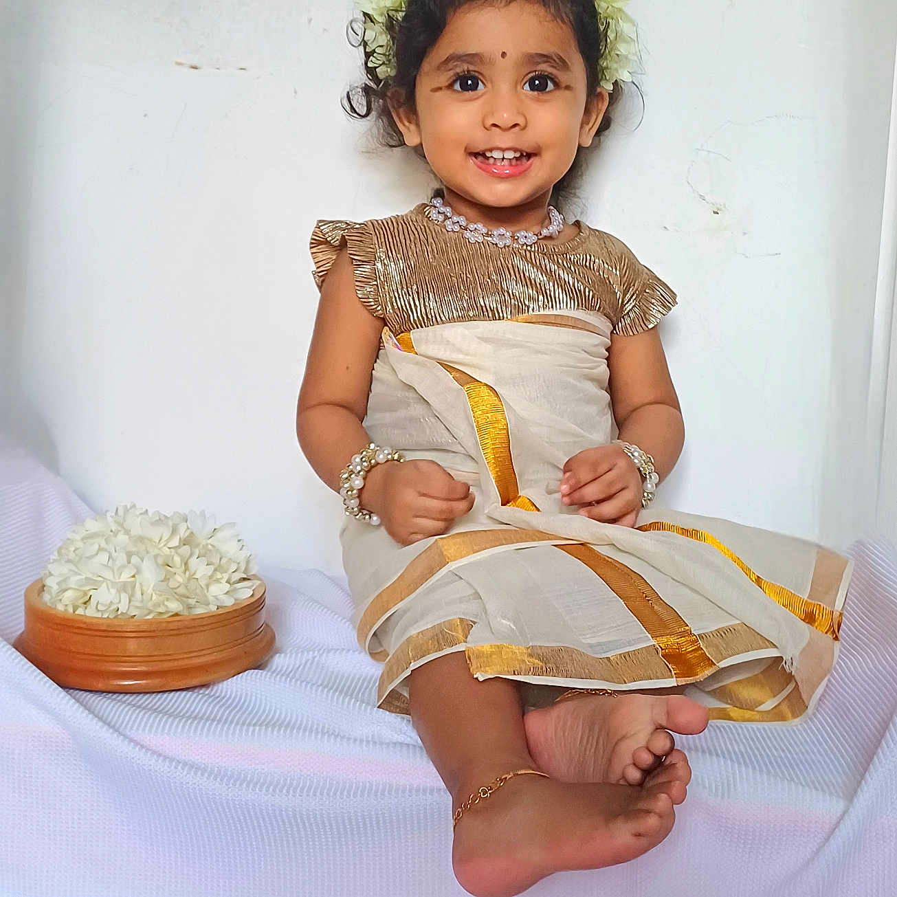 Kiara is registered to the contest to win money with this photo: accessories, anklet, barefoot, bowl, bracelet, child, cute, flower_crown, flowers, girl, gold_trim, happy, indoor, pearls, portrait, sitting, smiling, toddler, traditional_clothing, white_background
