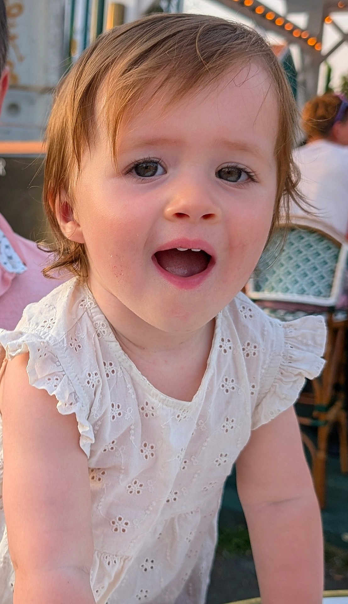Sharlie a rejoint le concours — aidez-le/la à gagner de superbes lots ! toddler, child, smiling, white_dress, outdoor, portrait, happy, face, cute, young_child, person, embroidery, candid, daylight, expression, eyes, hair, skin, restaurant, chair
