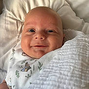 Oakley is registered to the contest to win money with this photo: baby, infant, smile, blanket, pillow, white, cute, child, face, soft, cozy, sleepwear, lying_down, portrait, indoors, newborn, happy, closeup, skin, head