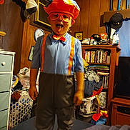 Sebastian joined the competition — help win amazing prizes! child, costume, orange, hat, suspenders, tongue_out, indoor, bookshelf, trophies, clutter, furniture, television, clothing, person, room, playful, glasses, bed, basket, decor