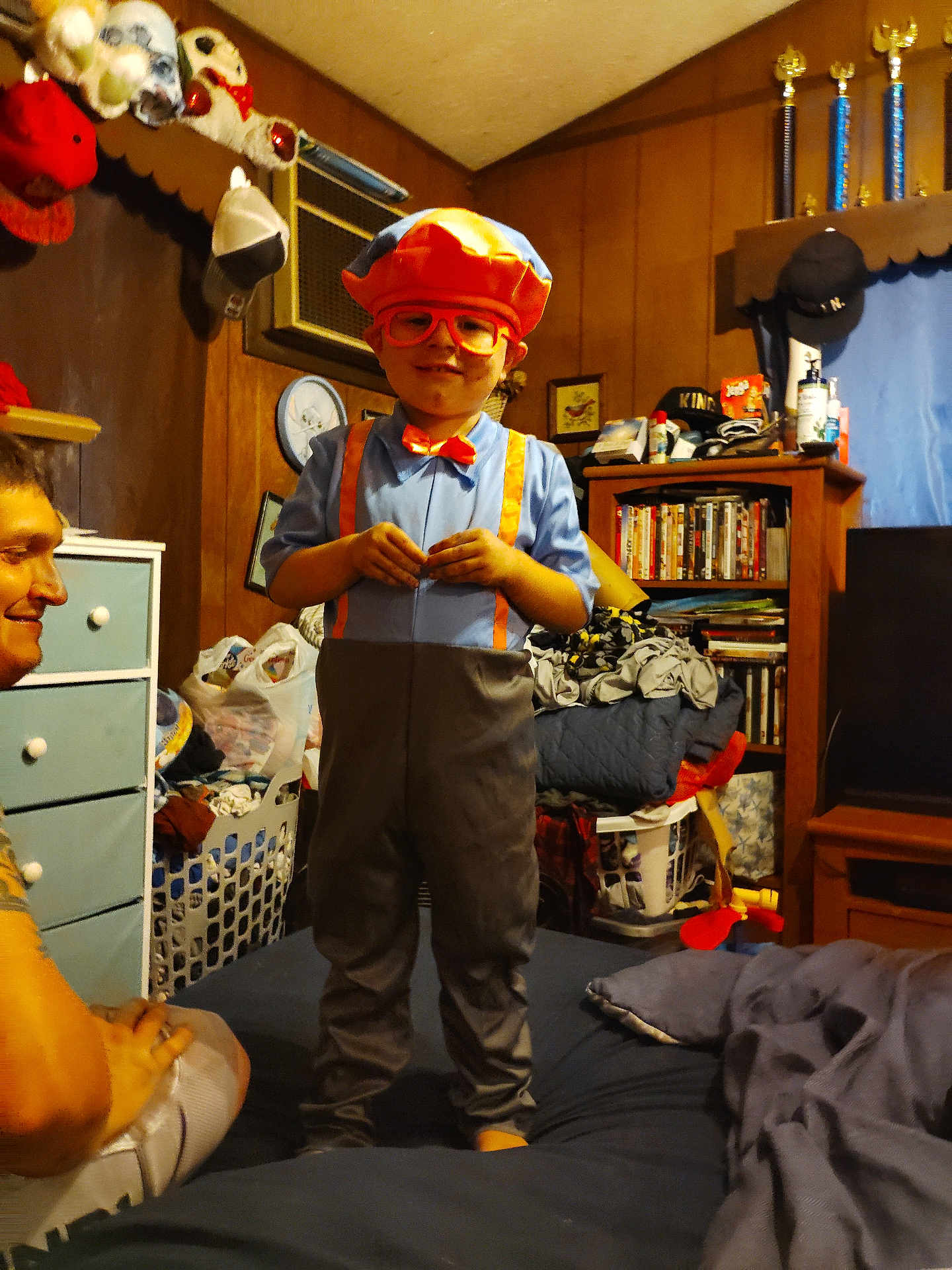 Sebastian is registered to the contest to win money with this photo: child, costume, orange, glasses, bedroom, adult, smile, furniture, laundry, shelf, dvds, toy, hat, bow_tie, suspenders, person, indoor, clothing, room, face