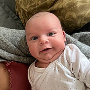 Fabio participe au concours pour gagner de l'argent avec cette photo : baby, infant, smile, face, onesie, blanket, cushion, pattern, cozy, chubby_cheeks, cute, indoors, person, portrait, head, expression, newborn, clothing, closeup, happy