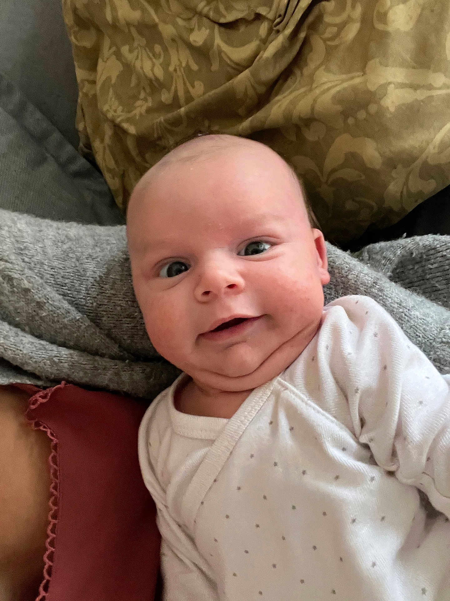 Fabio participe au concours pour gagner de l'argent avec cette photo : baby, infant, smile, face, onesie, blanket, cushion, pattern, cozy, chubby_cheeks, cute, indoors, person, portrait, head, expression, newborn, clothing, closeup, happy