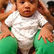 Journey joined the competition — help win amazing prizes! baby, child, infant, person, face, hair_bows, green_pants, white_onesie, sitting, indoor, curious, wide_eyes, hands, legs, background, blurred, cozy, cute, expression, skin