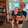 baby, infant, adult, woman, smiling, happy, portrait, indoors, home, family, holding, arms, bookshelf, books, toy, window, kitchen, clothing, glasses, cap