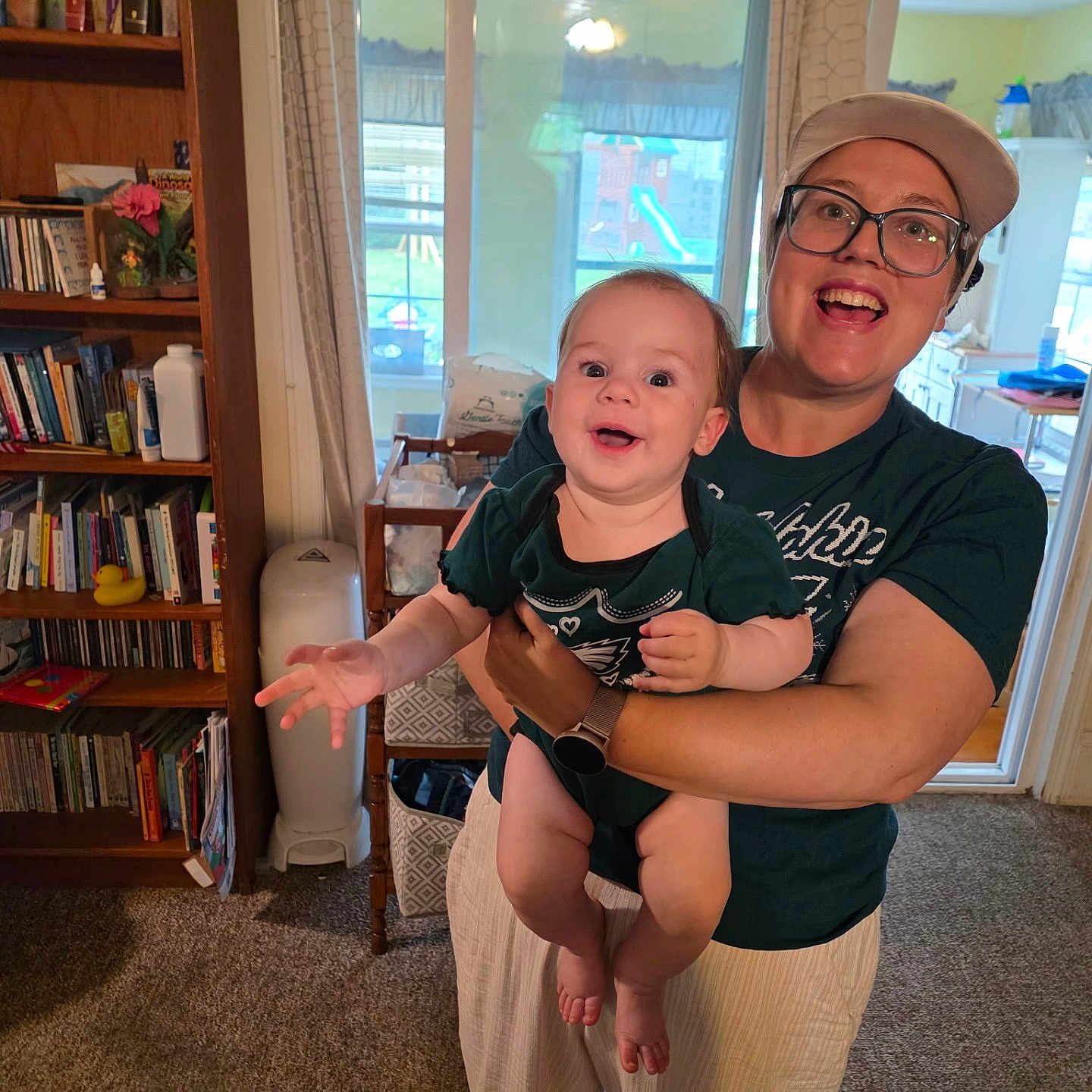 Hannah is registered to the contest to win money with this photo: baby, infant, adult, woman, smiling, happy, portrait, indoors, home, family, holding, arms, bookshelf, books, toy, window, kitchen, clothing, glasses, cap