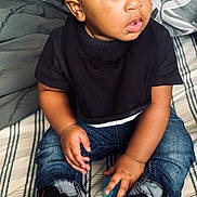 Bryce is registered to the contest to win money with this photo: toddler, child, afro_hair, black_shirt, ripped_jeans, sneakers, bedspread, striped_bedspread, blue_ball, indoor, curious_expression, seated, hands, young_child, casual_clothing, footwear, portrait, home, person, looking_away