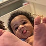 baby, child, curly_hair, tongue_out, feet, close_up, indoor, playful, person, cute, expression, skin, hand, red_clothing, background, head, face, foot, infant, young_child