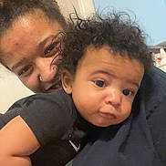 Leo is registered to the contest to win money with this photo: baby, child, woman, face, curly_hair, indoor, smile, closeup, person, skin, black_clothing, holding, portrait, young_child, nose_ring, home, candid, expression, light_skin, dark_skin