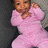 baby, child, smiling, pink_pajamas, heart_pattern, couch, pillow, indoor, happy, infant, cute, portrait, sitting, cozy, person, clothing, hand, face, head, young