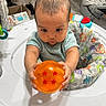 Selena is registered to the contest to win money with this photo: baby, child, toy, orange, dragon_ball, four_stars, baby_seat, colorful, indoor, curious, holding, infant, floor, wooden_floor, clothing, short_sleeve, face, hands, play, home