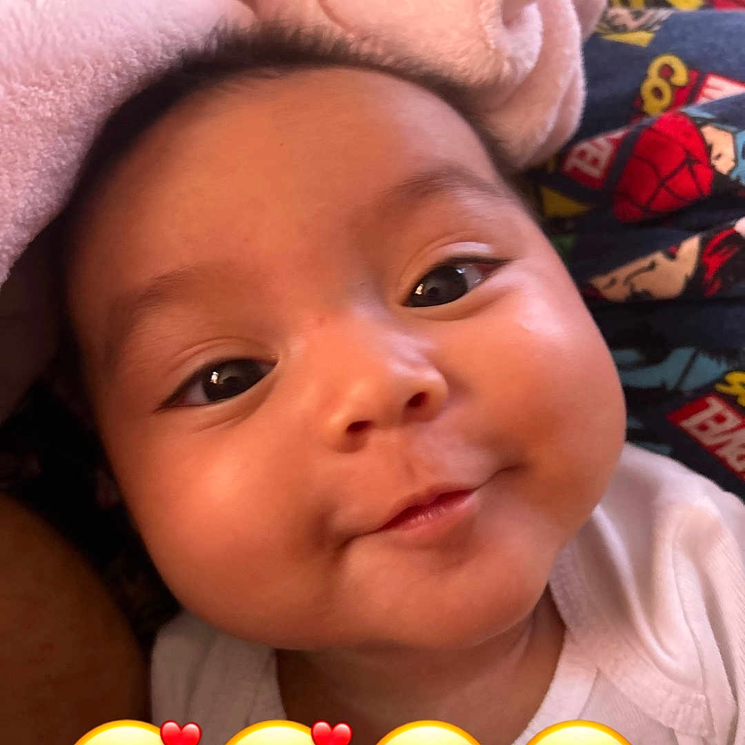 Selena joined the competition — help win amazing prizes! baby, face, smile, child, blanket, cozy, cute, closeup, infant, chubby_cheeks, superhero_pattern, colorful, eyes, expression, indoors, soft_texture, happy, adorable, head, portrait