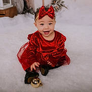 Lovelyn is registered to the contest to win money with this photo: baby, child, red_dress, headband, bow, smiling, holiday, christmas_ornament, festive, fluffy_surface, black_shoes, indoor, cute, portrait, happy, toddler, celebration, seasonal, decor, sitting