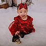 baby, child, red_dress, headband, bow, smiling, holiday, christmas_ornament, festive, fluffy_surface, black_shoes, indoor, cute, portrait, happy, toddler, celebration, seasonal, decor, sitting