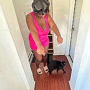 Odem joined the competition — help win amazing prizes! animal, black_cat, bonnet, casual, cat, curious_cat, door, flooring, hallway, home, indoor, interaction, person, pet, pink_dress, playful, slippers, standing, white_wall, wooden_floor