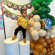 Gino joined the competition — help win amazing prizes! toddler, child, birthday, party, balloons, minecraft, yellow_shirt, black_pants, boots, banner, indoor, celebration, decorations, standing, pedestal, smiling, festive, face, person, event