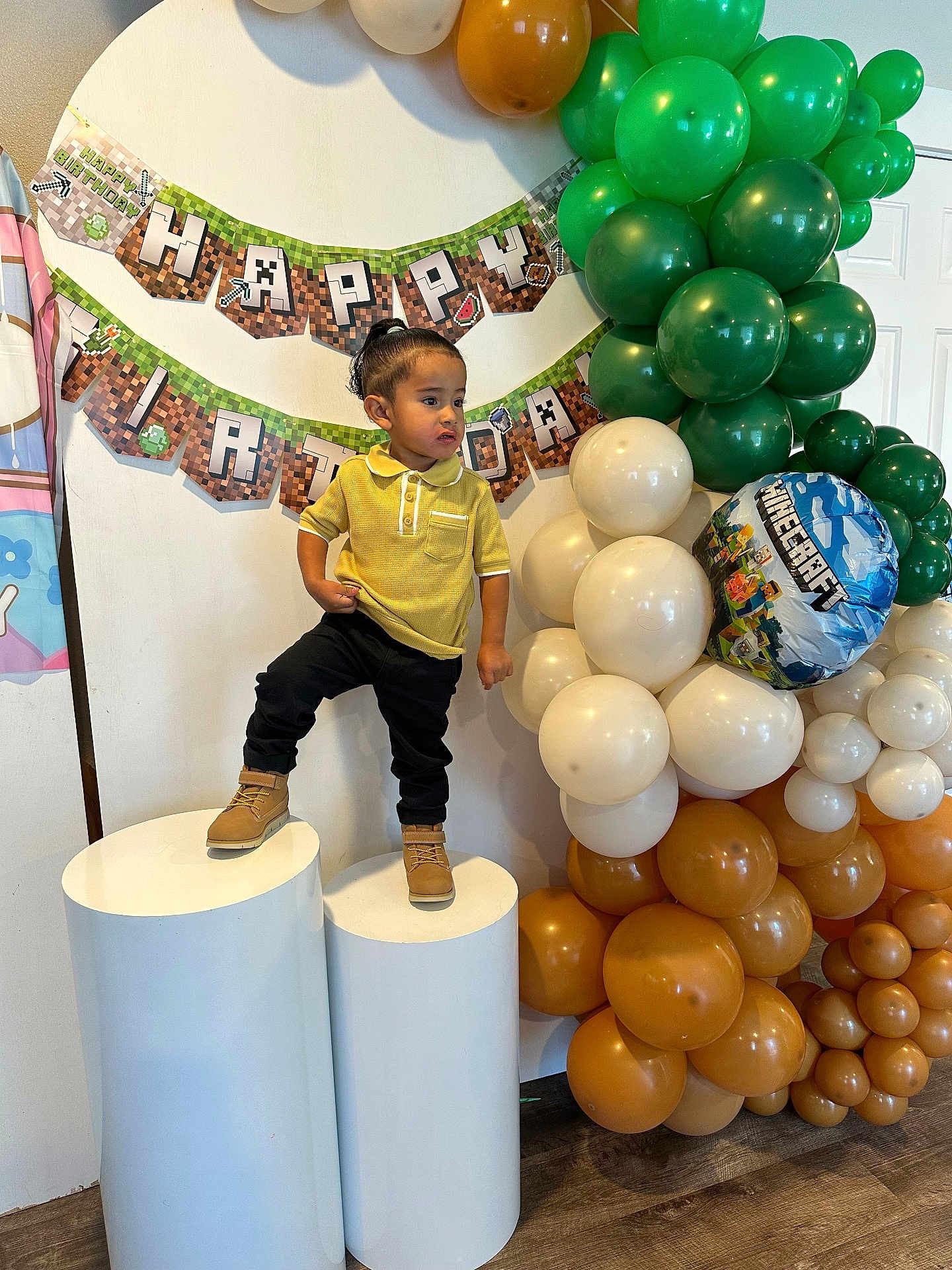 Gino joined the competition — help win amazing prizes! toddler, child, birthday, party, balloons, minecraft, yellow_shirt, black_pants, boots, banner, indoor, celebration, decorations, standing, pedestal, smiling, festive, face, person, event