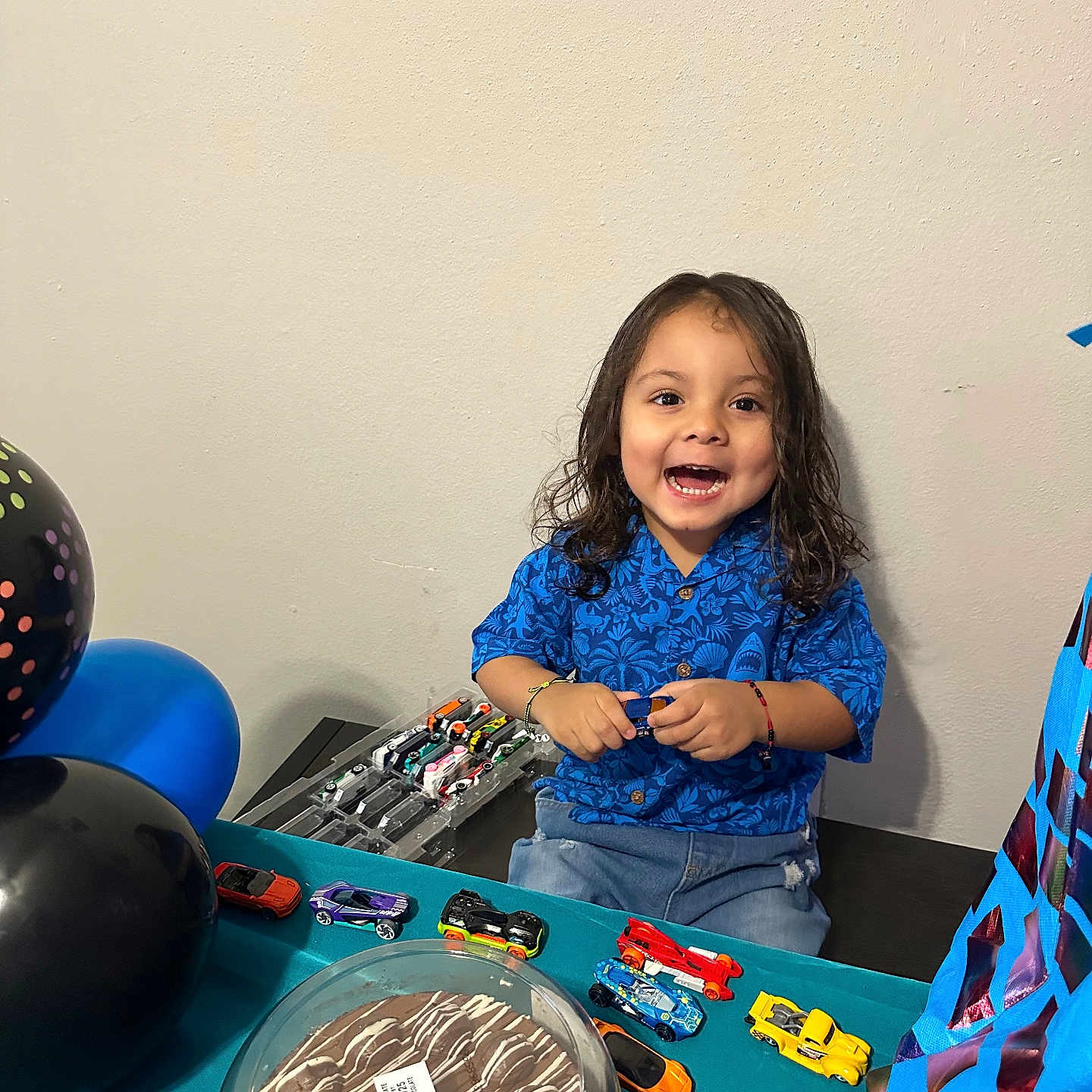 Matias Gabriel joined the competition — help win amazing prizes! balloons, birthday, blue_shirt, cake, celebration, child, chocolate_cake, curly_hair, decorations, fun, happy, indoor, jeans, party, person, play, smiling, table, toddler, toy_cars