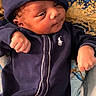 baby, infant, newborn, clothing, onesie, hat, polo_logo, face, hand, fist, blanket, pattern, blue, navy, lying_down, sleepy, cute, portrait, indoors, cozy