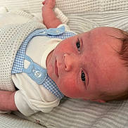 Theo is registered to the contest to win money with this photo: baby, infant, face, skin, blue_eyes, clothing, blanket, fabric, cushion, white, blue, newborn, lying_down, portrait, closeup, person, cute, sleepwear, indoors, soft_lighting