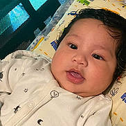 Zeno is registered to the contest to win money with this photo: baby, infant, face, onesie, pillow, cute, close_up, indoors, child, sleeping_area, cartoon_print, black_hair, soft_lighting, curious_expression, newborn, person, portrait, resting, baby_clothes, lying_down