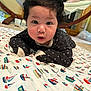 baby, infant, face, curly_hair, blanket, pattern, boats, indoor, floor, hammock, fireplace, wooden_furniture, cute, expression, clothing, long_sleeves, tummy_time, person, child, home