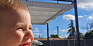 Joey a rejoint le concours — aidez-le/la à gagner de superbes lots ! baby, child, smile, laughing, outdoor, blue_sky, clouds, sunlight, backyard, patio, pergola, swing_set, hand, clothing, cheeks, portrait, happy, weekend, play, person