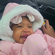 Chloe is registered to the contest to win money with this photo: adorable, baby, car_seat, closeup, cozy, dark_skin, eye_contact, fur_trim, hand, hood, infant, joyful, mouth_open, pink_jacket, portrait, smile, smiling, star_pattern, teeth, winter_clothing