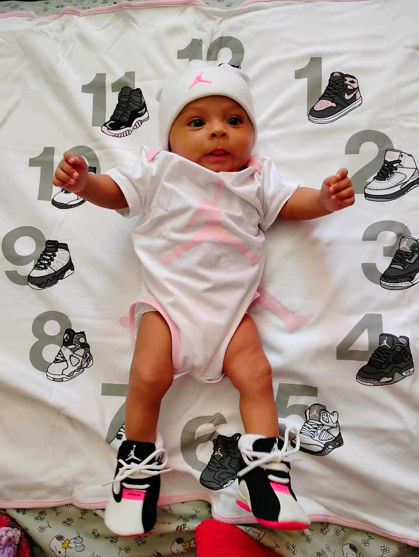 Jordyn is registered to the contest to win money with this photo: baby, infant, onesie, beanie, sneakers, baby_shoes, blanket, numbers, print, pink, white_background, legs, feet, lying_down, cute, eyes_open, smile, playmat, textile, pattern