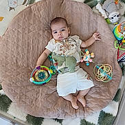 Noah is registered to the contest to win money with this photo: baby, child, toys, cushion, blanket, soft, indoor, infant, playtime, cute, comfort, lying_down, colorful, expression, clothing, floor, relaxing, person, young_child, peaceful