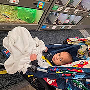 Dallas is registered to the contest to win money with this photo: baby, blanket, stroller, child, indoor, pet_store, animal_enclosure, car_pattern, curious, flooring, toy, hay, glass, small_animal, person, clothing, face, seated, wheel, colorful