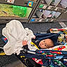baby, blanket, stroller, child, indoor, pet_store, animal_enclosure, car_pattern, curious, flooring, toy, hay, glass, small_animal, person, clothing, face, seated, wheel, colorful