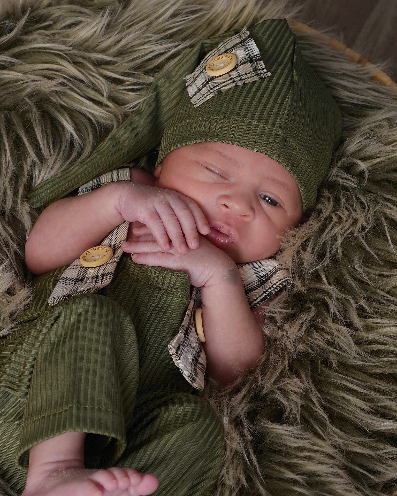 Dallas joined the competition — help win amazing prizes! baby, newborn, infant, sleepy, green_outfit, hat, fur_blanket, cute, small_hands, small_feet, soft_texture, portrait, indoors, cozy, resting, child, one_eye_open, plaid_pattern, button, closeup