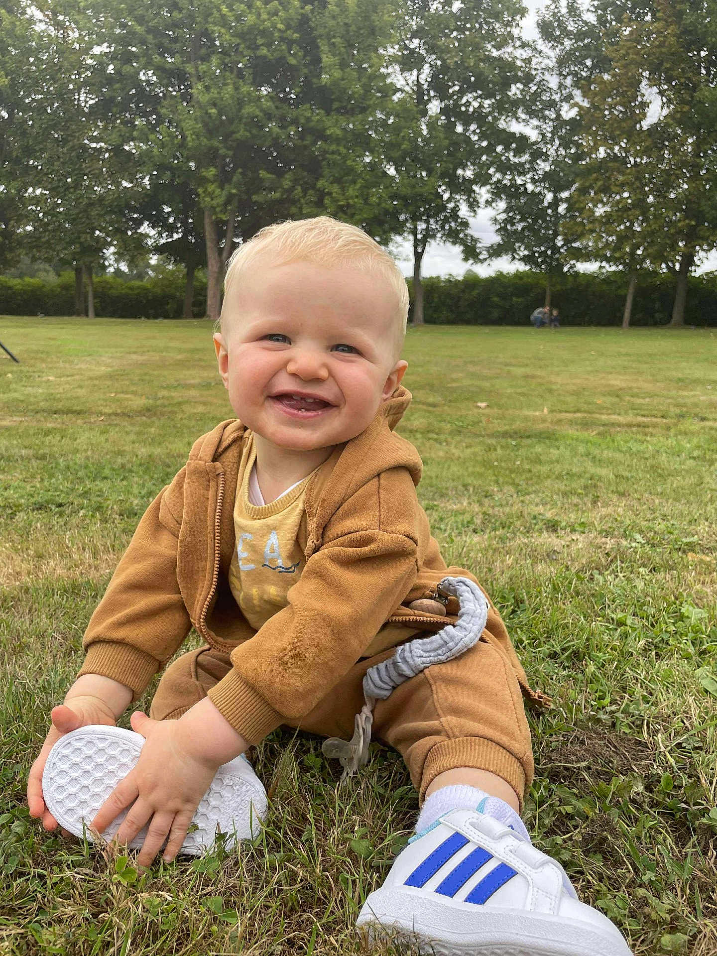 Albin a rejoint le concours — aidez-le/la à gagner de superbes lots ! toddler, child, smile, grass, shoe, sneaker, outdoor, park, trees, clothing, blond_hair, baby, happy, person, casual_wear, nature, daylight, sitting, cute, playful