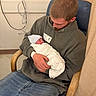 newborn, baby, child, father, parent, hospital, hospital_room, chair, swaddled, blanket, hat, portrait, family, holding, sleeping, infant, medical_equipment, curtain, hoodie, newborn_photography