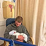 Matteo is registered to the contest to win money with this photo: baby, newborn, infant, father, parent, hospital, swaddled, blanket, chair, medical_equipment, hospital_room, curtain, family, parenting, holding, sitting, hoodie, jeans, portrait, birth