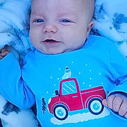 Robbie is registered to the contest to win money with this photo: baby, infant, smiling, blue_shirt, red_truck, blanket, cozy, cute, child, portrait, happy, clothing, lying_down, indoors, soft_texture, young, face, small_hand, casual, comfort