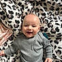 Louka participe au concours pour gagner de l'argent avec cette photo : baby, smiling, infant, child, grey_clothing, ribbed_fabric, blanket, floral_pattern, black_and_white, pink_accents, happy, cute, portrait, lying_down, hand, head, face, skin, indoors, soft_light