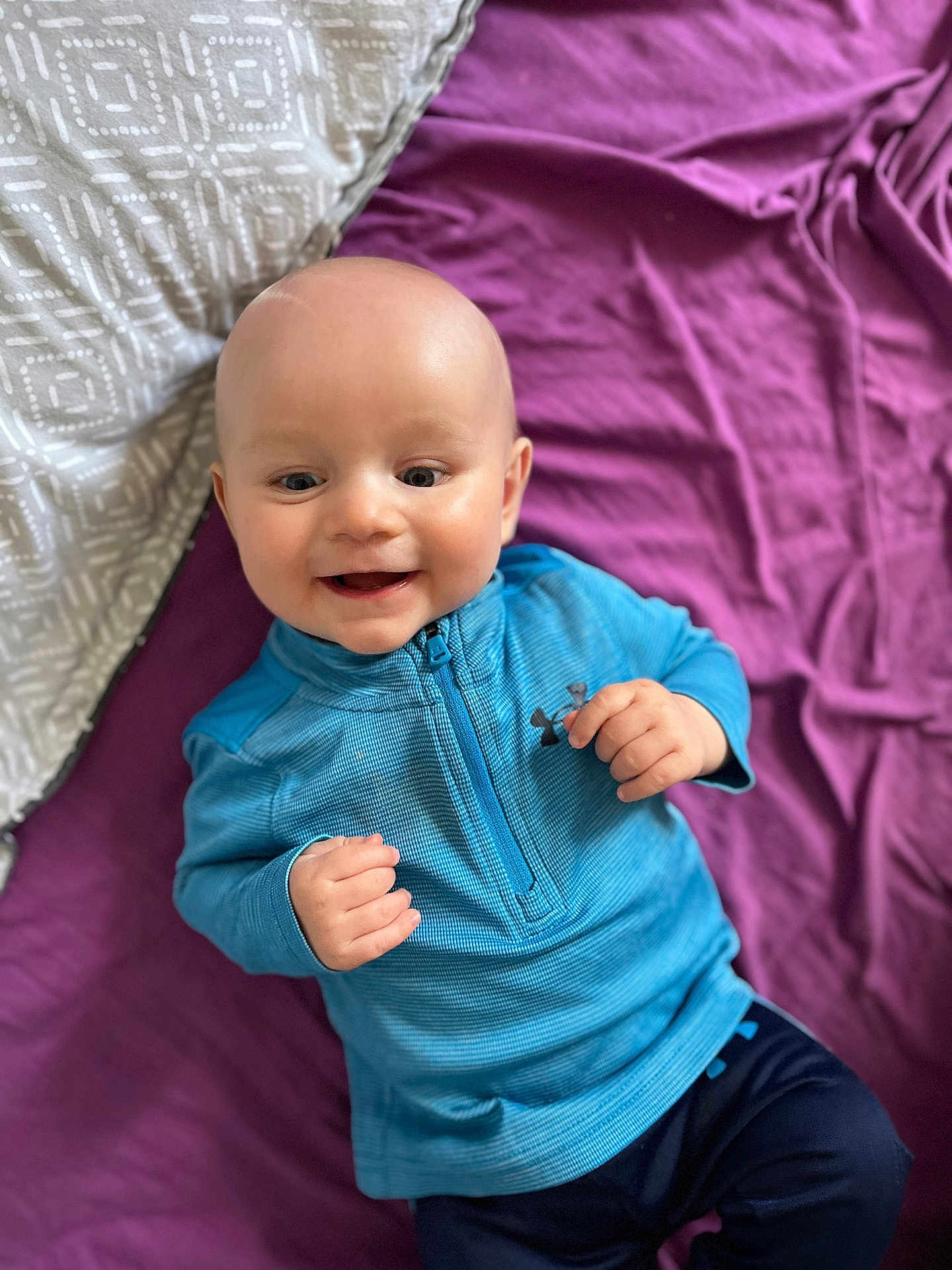 Louka participe au concours pour gagner de l'argent avec cette photo : baby, smiling, blue_clothing, bald_head, pillow, blanket, lying_down, infant, happy, child, face, person, indoor, cute, young, portrait, sleeve, fabric, zipper, fingertips