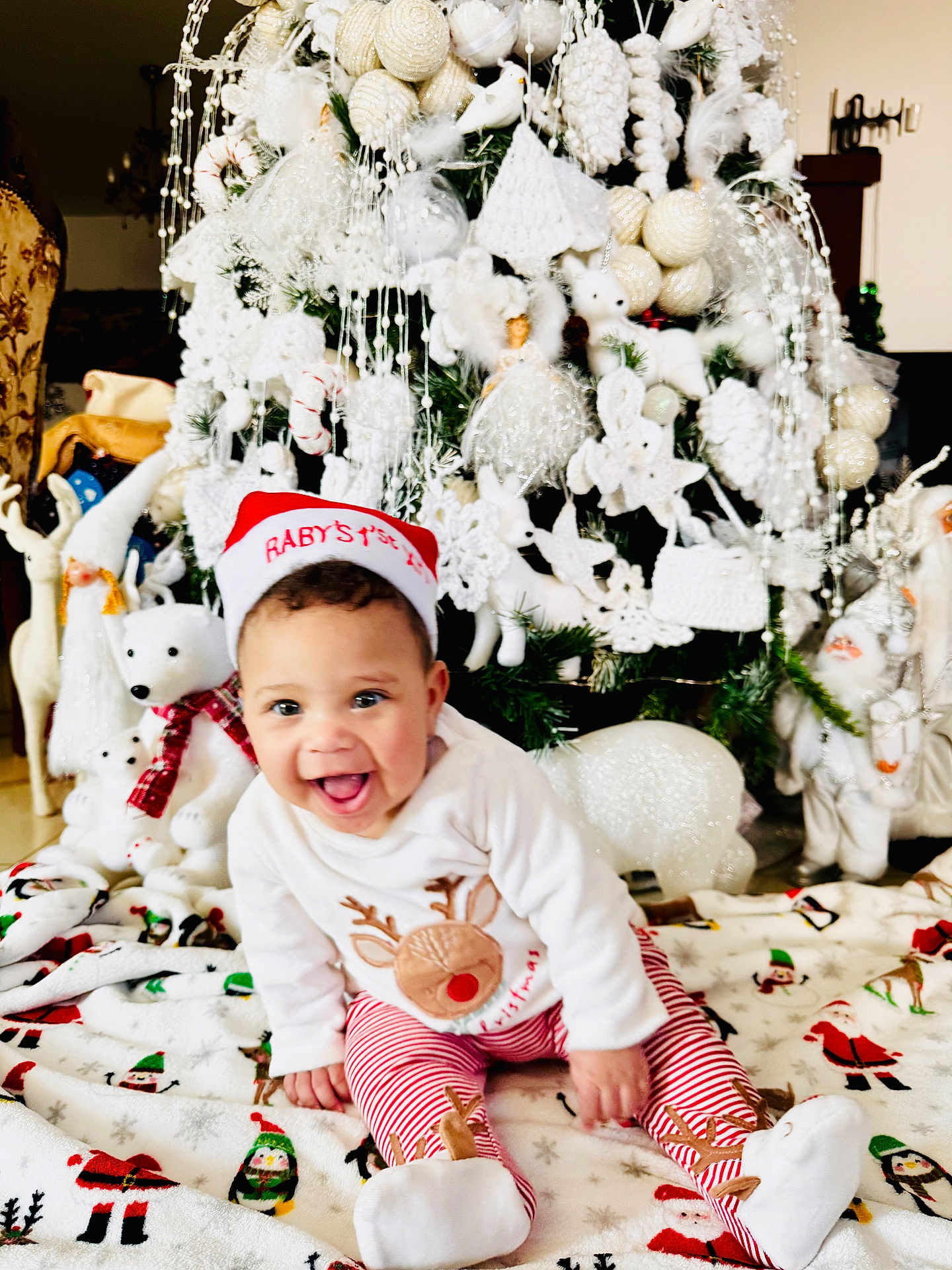 Christina is registered to the contest to win money with this photo: baby, child, christmas_tree, holiday, festive, santa_hat, plush_toys, polar_bear, decorations, blanket, smiling, indoors, red_and_white, striped_pants, reindeer, happy, cute, celebration, christmas, winter