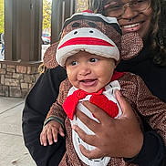 Dandre joined the competition — help win amazing prizes! baby, child, costume, sock_monkey, adult, glasses, smile, outdoor, person, holding, joyful, happy, face, hand, clothing, hood, portrait, daylight, building, window