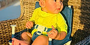 Adrián is registered to the contest to win money with this photo: baby, child, yellow_clothing, blue_chair, wicker_chair, outdoor, sunlight, skin, feet, hands, face, curious, pensive, seatbelt, summer, daytime, infant, portrait, sitting, baby_chair