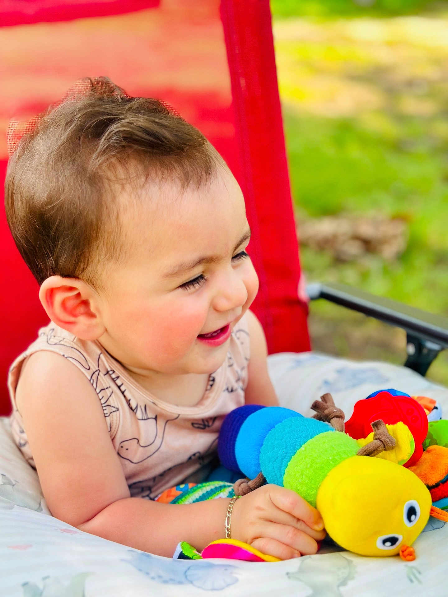 Adrián is registered to the contest to win money with this photo: toddler, child, toy, plush, caterpillar, smiling, happy, outdoor, red_chair, cushion, clothing, bracelet, person, portrait, cute, baby, nature, seat, playful, fun
