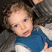 Theo participe au concours pour gagner de l'argent avec cette photo : toddler, child, curly_hair, blue_eyes, blue_vest, white_shirt, bed, bedding, indoor, portrait, face, cute, infant, person, baby, young_child, sleeping_area, headboard, curiosity, closeup