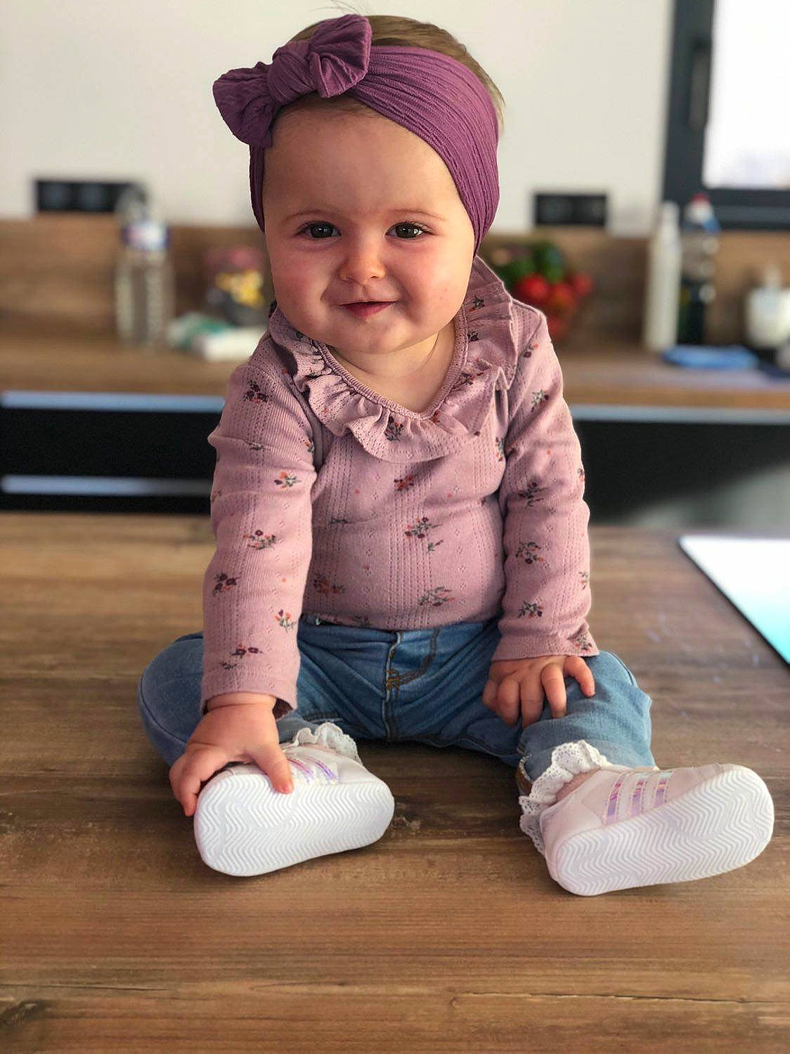 Marëva participe au concours pour gagner de l'argent avec cette photo : baby, baby_toddler_clothing, cap, cheek, child, face, floor, flooring, foot, fun, happy, hardwood, joy, person, sitting, skin, sleeve, smile, standing, toddler