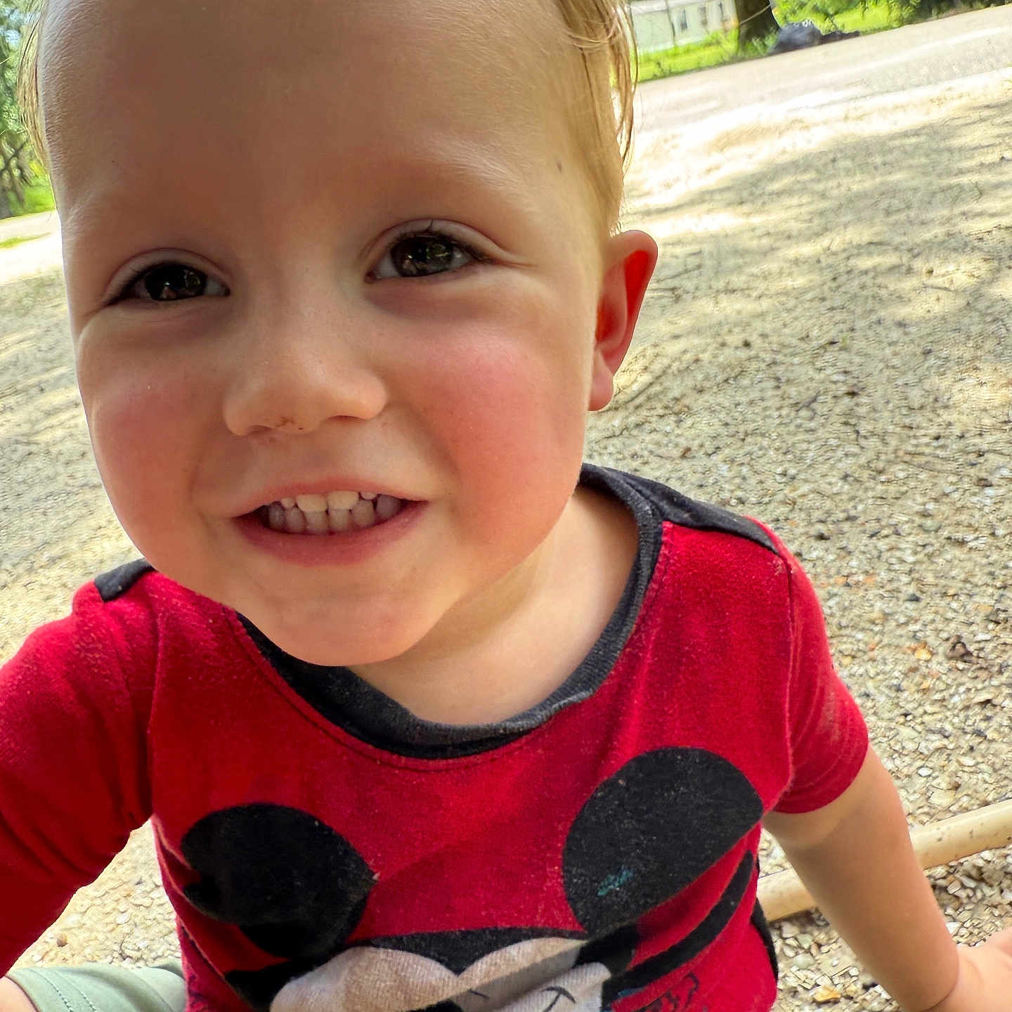 Ilias is registered to the contest to win money with this photo: casual_clothing, child, closeup, cute, daylight, face, gravel, greenery, happy, mickey_mouse, nature, outdoor, person, playful, red_shirt, smiling, summer, toddler, trees, young_child