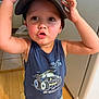 arms, cap, casual, child, clothing, cute, expression, face, floor, hat, indoor, kitchen, person, portrait, standing, tank_top, toddler, toy_car_graphic, wooden_floor, young_child